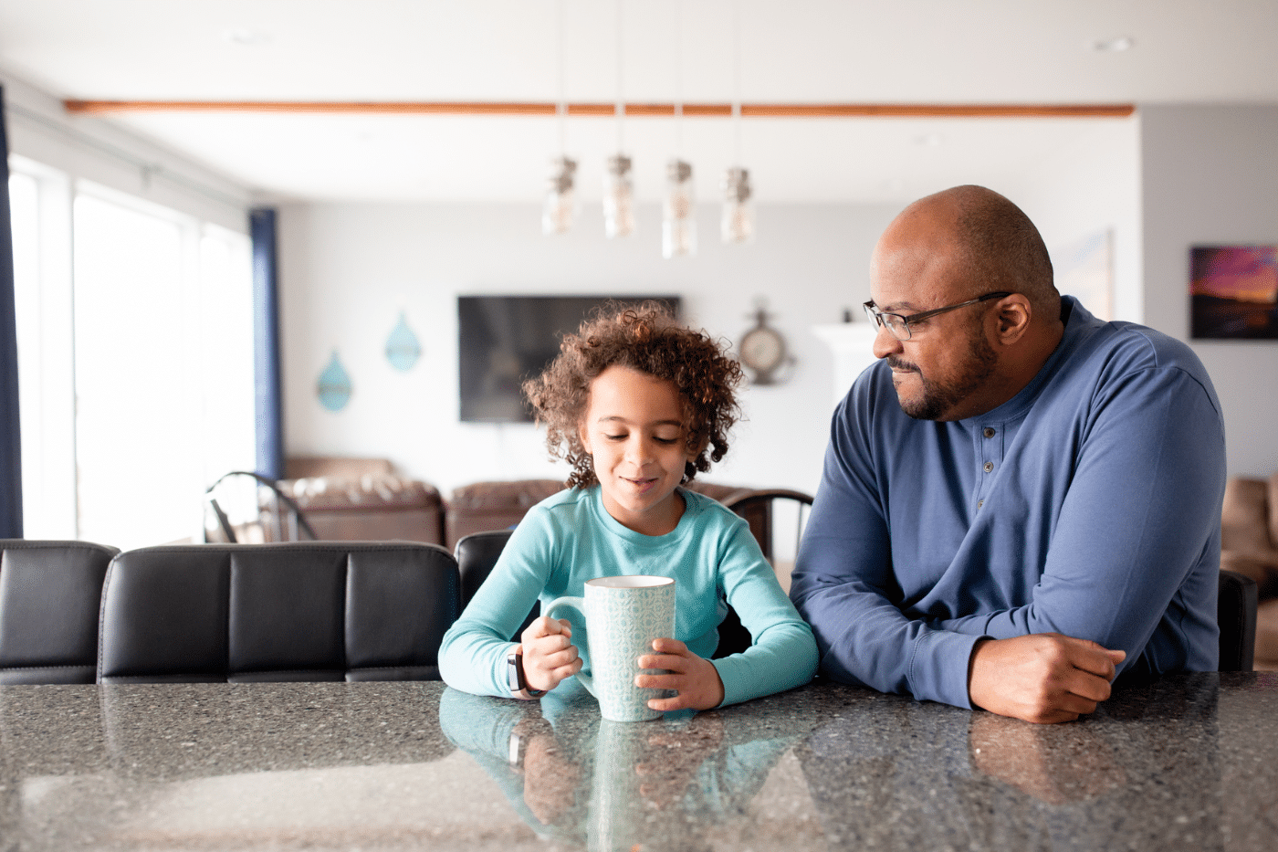 Father And Daughter Sit Together At Breakfast Bar With Drink