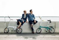 Young people posing on fence of bridge embracing near bicycles