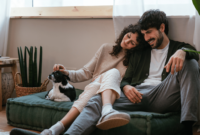 Smiling loving couple relaxing on sofa and caressing small Chihuahua dog while spending time together at home