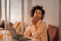 Remote working candid portrait of African beautiful pensive young woman with laptop in cafeteria.