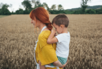 Side view of a woman walking in the field, holding her son on her back